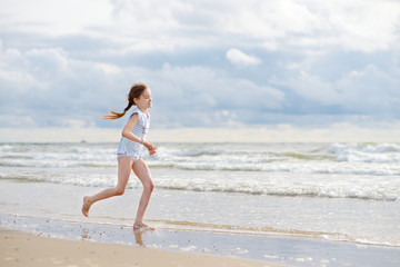 Cute little girl having fun on a sandy beach on warm and sunny summer day. Kid playing by the ocean.