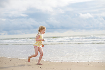 Fototapeta na wymiar Cute little girl having fun on a sandy beach on warm and sunny summer day. Kid playing by the ocean.