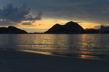 Dusk on the beach of San Francisco, Niteroi, Rio de Janeiro, Brazil. The sky is orange, the sea calm with the sun reflecting in the sea; you can see the silhouette of the mountains of the city of Rio.