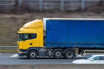 Yellow lorry with blue trailer in motion on the motorway