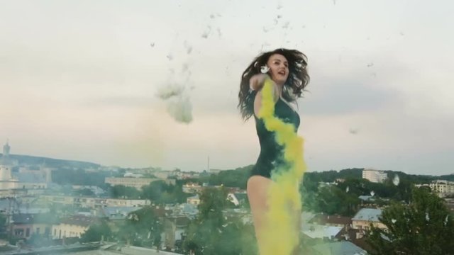 young brunette woman wearing bodysuit roof building lighting colored bomb yellow smoke joke fun jumping trampoline happy active lifestyle art studio fashionable girl entertainment RED 4K