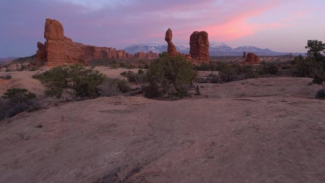 Rising view from behind rocks to view Balanced Rock in the Utah desert during colorful sunset.