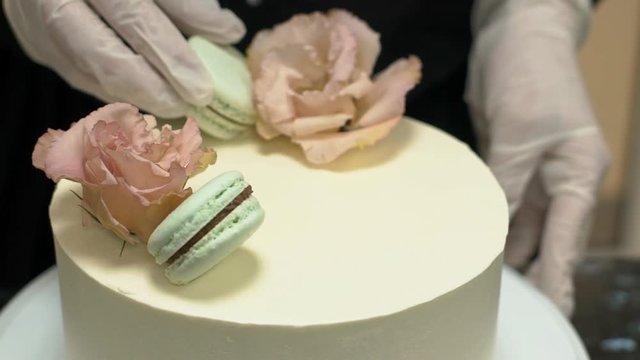 Close up of cheese cake being decorated with roses and lime cookies in confectionery shop. Baker is working in black uniform and in white gloves to make a delicious sweet dessert for celebration. slow