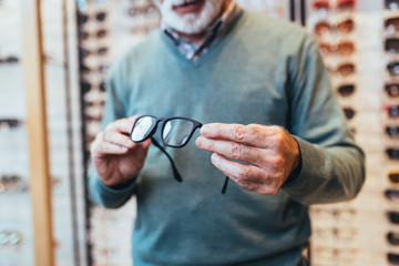 Handsome senior man choosing eyeglasses frame in optical store. 