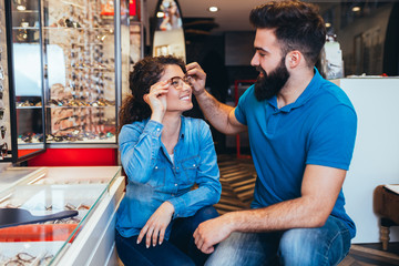 Happy young couple choosing together eyeglasses frame in optical store. 