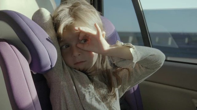 Funny girl sits in a moving car and keeps an OK gesture at her eye