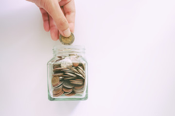 Hand saving a coin into the glass jar on white background with for business and finance concept (added colour filter)