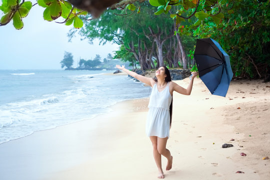 Woman in white dress on beach holding umbrella enjoying rain