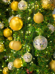 Obraz na płótnie Canvas Golden and glitter bauble balls hanging from a decorated Christmas tree with yellow light decored. Selective Focus.