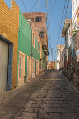 Narrow, hilly stone paved street, with colorful houses and other architectural details, in Guanajuato, Mexico - 191813109