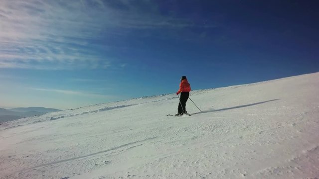 Woman in bright orange sportswear is skiing on the slope of hill at sunny winter day