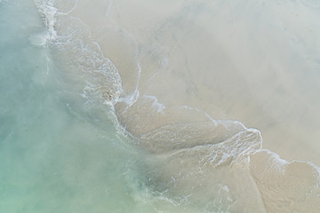 Blick von oben auf Strand mit türkisem Meer und Welle