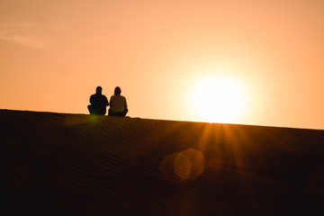 Paar sitzt auf der Düne in der Wüste und schaut in den Sonnenuntergang