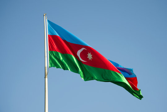 The national flag of Azerbaijan is flying in the blue sky