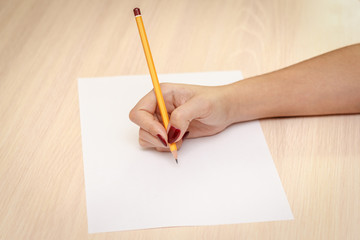 Woman's hand with pencil writing on paper on wooden table background