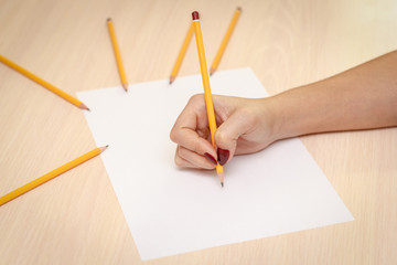 Woman's hand with pencil writing on paper on wooden table background