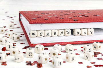 Women's Day greeting message written in wooden blocks in red notebook on white table.