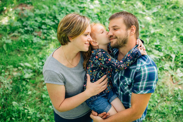 Fototapeta premium Cute young happy family having fun in the park. Little girl with parents outdoors. Mother father and daughter.