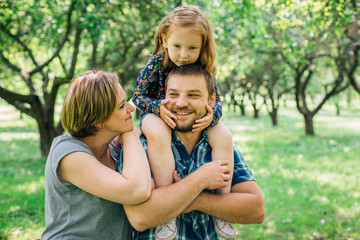 Fototapeta premium Cute young happy family having fun in the park. Little girl with parents outdoors. Mother father and daughter.