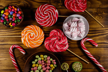 Colorful chocolate candies, lollipops, candy cane and marshmallows on wooden table
