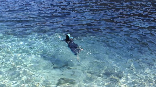 A Muslim woman is swimming in the sea.