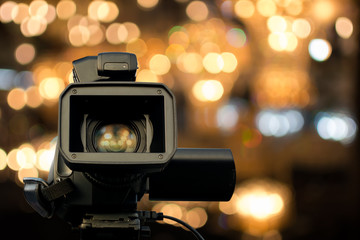 Front view of video camera with light reflection in lens and bokeh light in background. Selective focus.