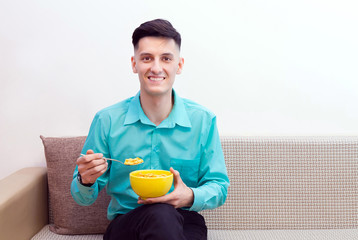 Portrait of a smiling young man in a green shirt holding a yellow bowl and a spoonful of cornflakes