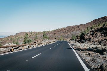 Highway goes through the rocks with green pine-trees to the right near the clouds. Teide National Park. Tenerife