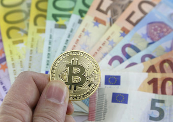 Hand with one big goden BITCOIN and euro banknotes