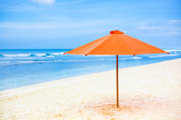 Fototapeta na wymiar Bright orange parasol on the sand beach. Blue sky and sea in the background
