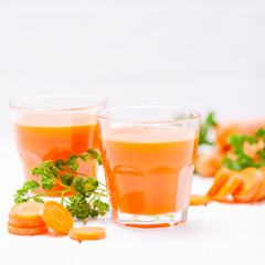 Carrot juice in beautiful glasses, cut orange vegetables and green parsley on white wooden background. Fresh orange drink. Close up photography. Selective focus. Horizontal banner