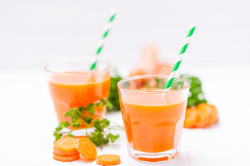 Carrot juice in beautiful glasses, cut orange vegetables and green parsley on white wooden background. Fresh orange drink. Close up photography. Selective focus. Horizontal banner