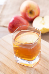 Apple cider vinegar in a glass cup, with apples on table.
