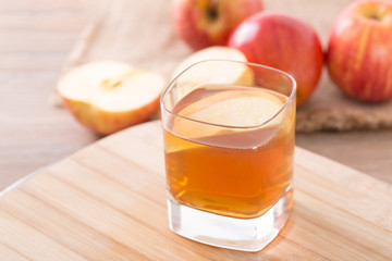 Apple cider vinegar in a glass cup, with apples on table.