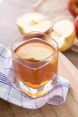 Apple cider vinegar in a glass cup, with apples on table.