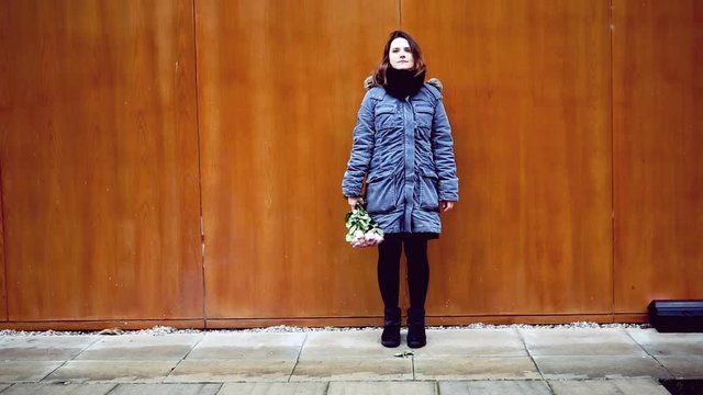 Cinemagraph of young woman standing at wooden wall with bouquet of roses
