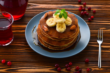 Pancakes with caramel, banana and nuts decorated with cranberries and mint with juice.