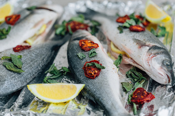 Raw fresh dorada fish and seabass with ingredients on foil ready for cooking. Lemon dried tomato and basil