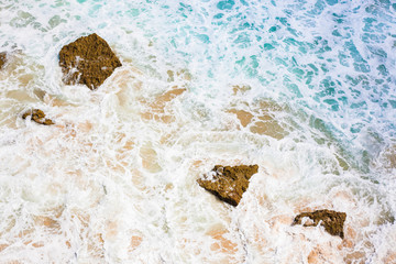 Fototapeta na wymiar Colorful wallpaper depicting raging ocean water with rocks and foam