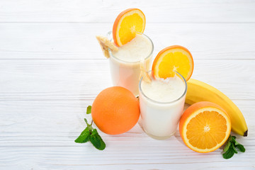 Smoothies with bananas and oranges, a sprig of mint on a white background. Space for text or design.