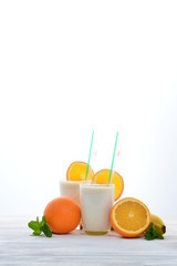 Smoothies with bananas and oranges, a sprig of mint on a white background. Space for text or design.
