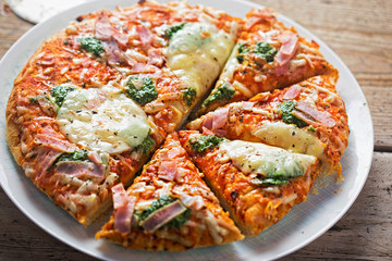 Pizza with green pesto, mozzarella, ham