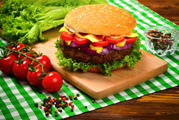 Delicious tasty burger with beef, tomatoes, salad and sauce on wooden table and black background.  Space for text or design.