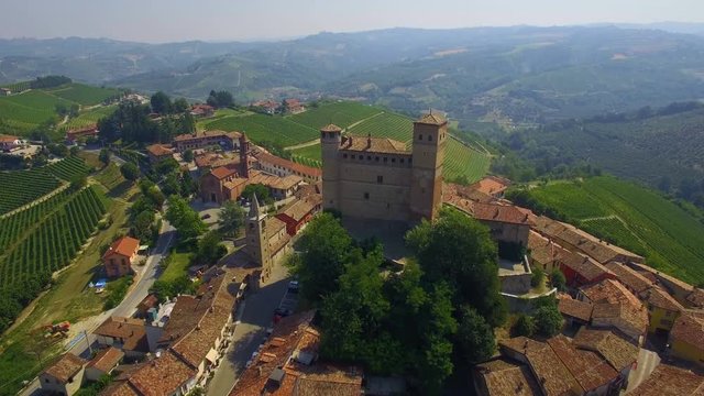 Aerial: slow flight over small Italian town - Serralunga d'Alba surrounded with vineyard hills. Piedmont region, Italy.