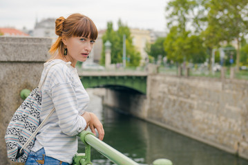 girl tourist walking around the city. Free travel. The girl near the water channel. young woman with a fun hairstyle travels alone with a backpack. Guided tour of Vienna
