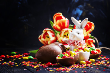 Easter composition with white rabbit, chocolate eggs and sweets, red tulips and colorful sugar, selective focus