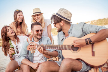 Group of young people listening to friend playing guitar outdoors