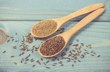 Ground cumin in a spoon and whole cumin on the wooden background.