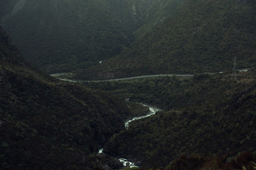 Paisaje montañoso en un día gris y oscuro con un río y una carretera atravesando la imagen