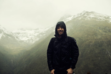 Retrato de hombre joven posando frente a paisaje de montañas nevadas nubladas.